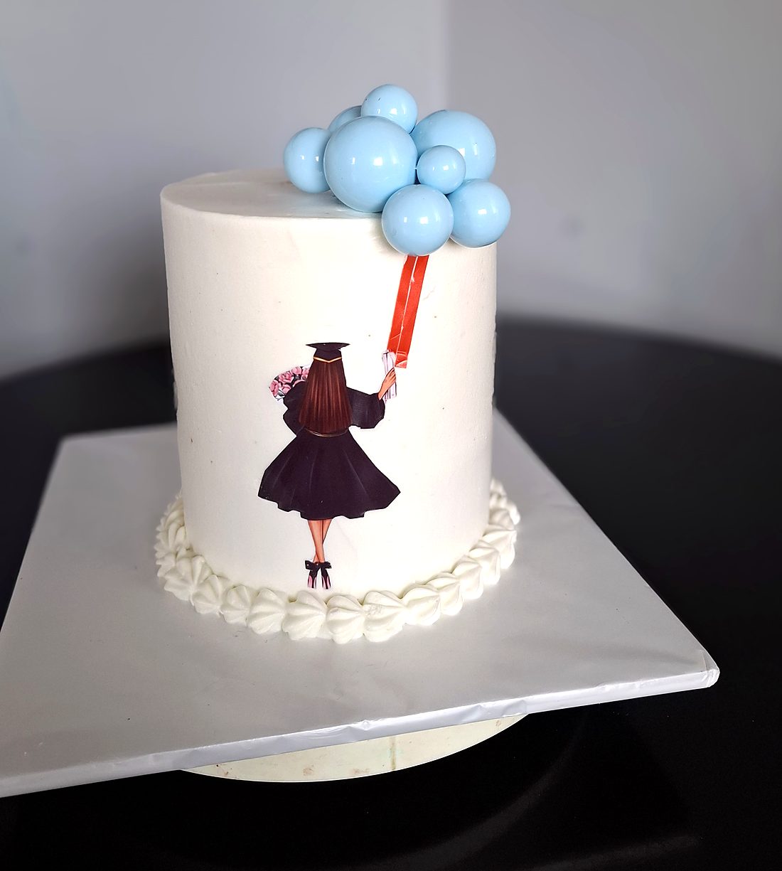 White graduation cake with a painted graduate holding a bunch of blue balloons
