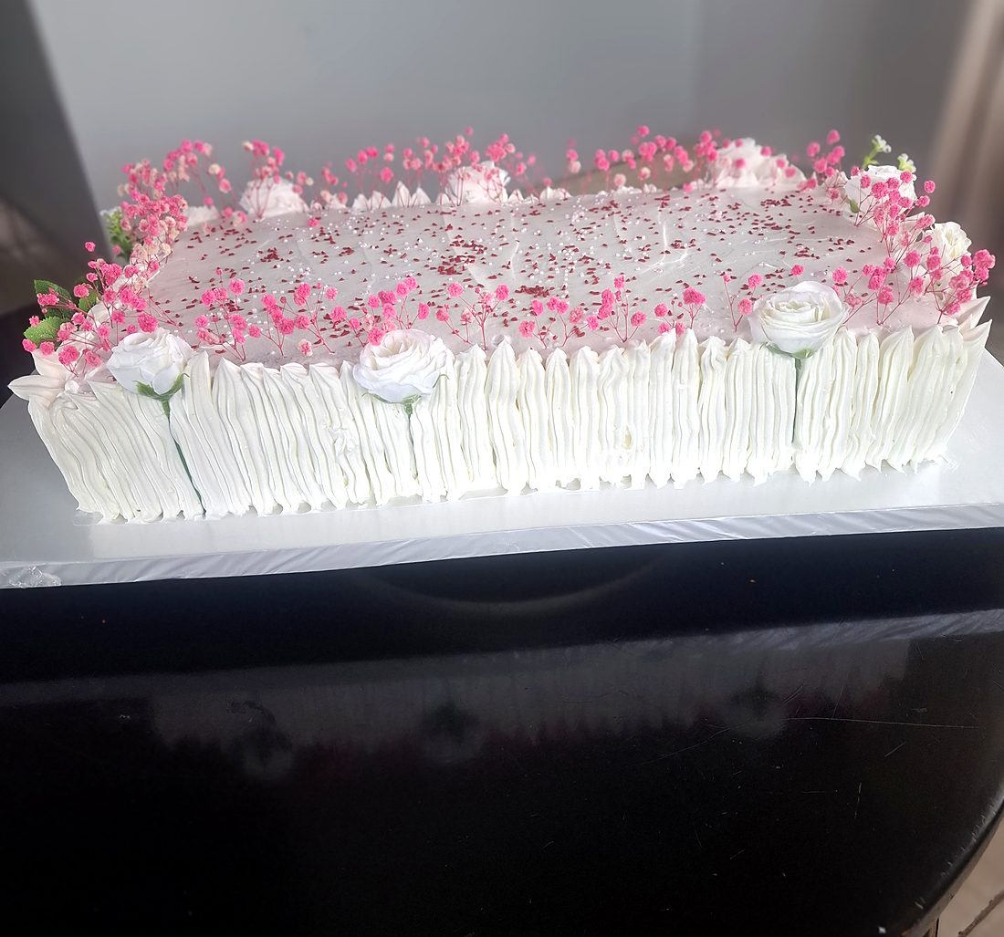 White sheet cake with pink sprinkles, piped roses and a white chocolate fence