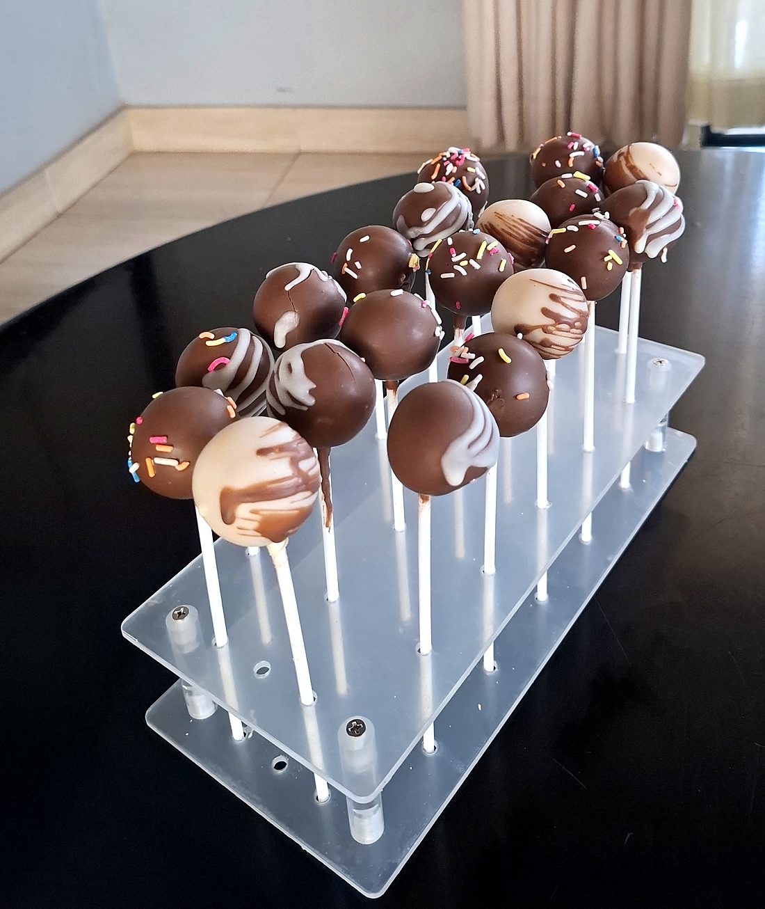 Chocolate cake pops with drizzle and sprinkles on a clear stand